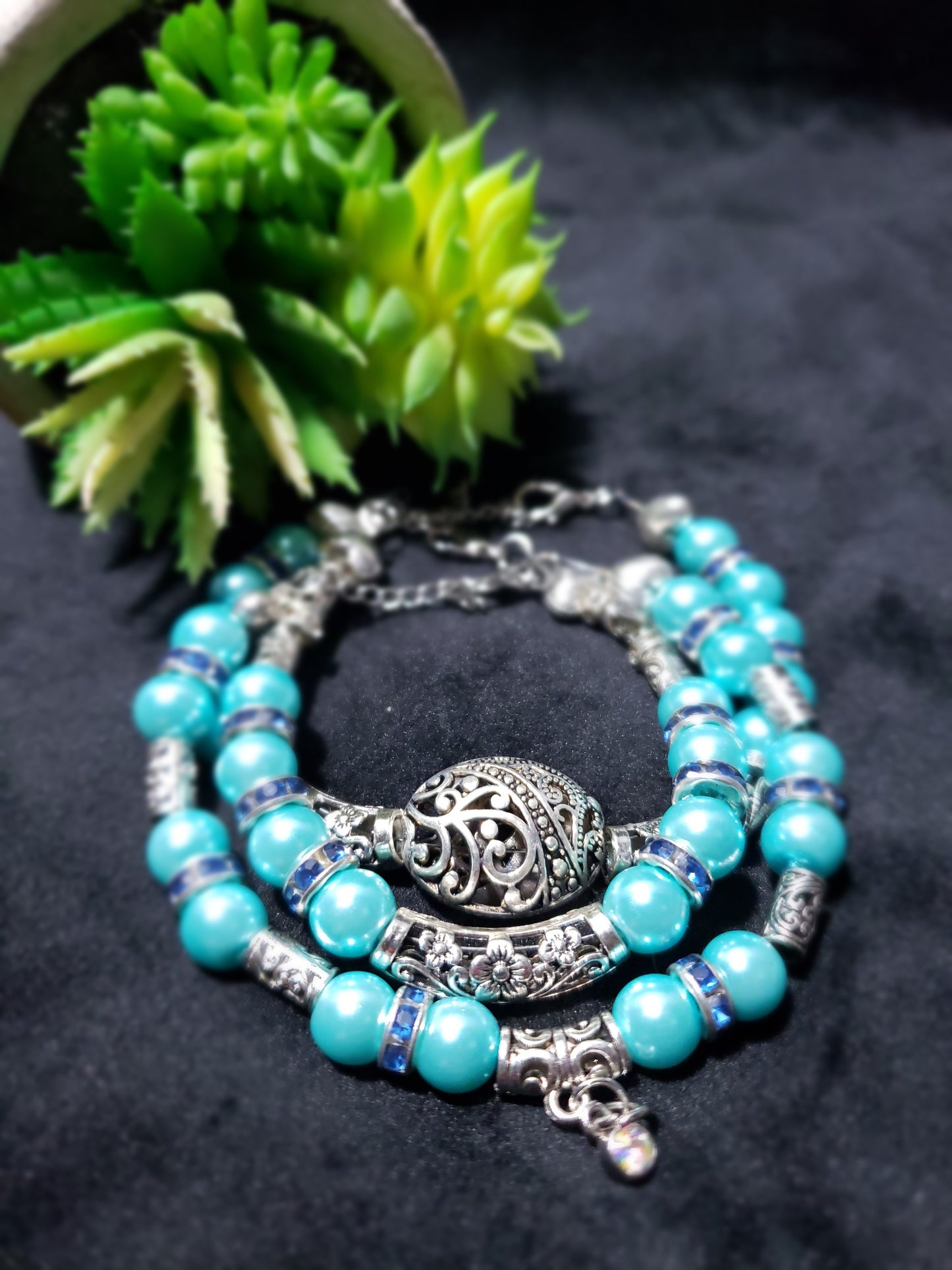 Blue beaded bracelet with silver accents on a dark surface with a green plant.