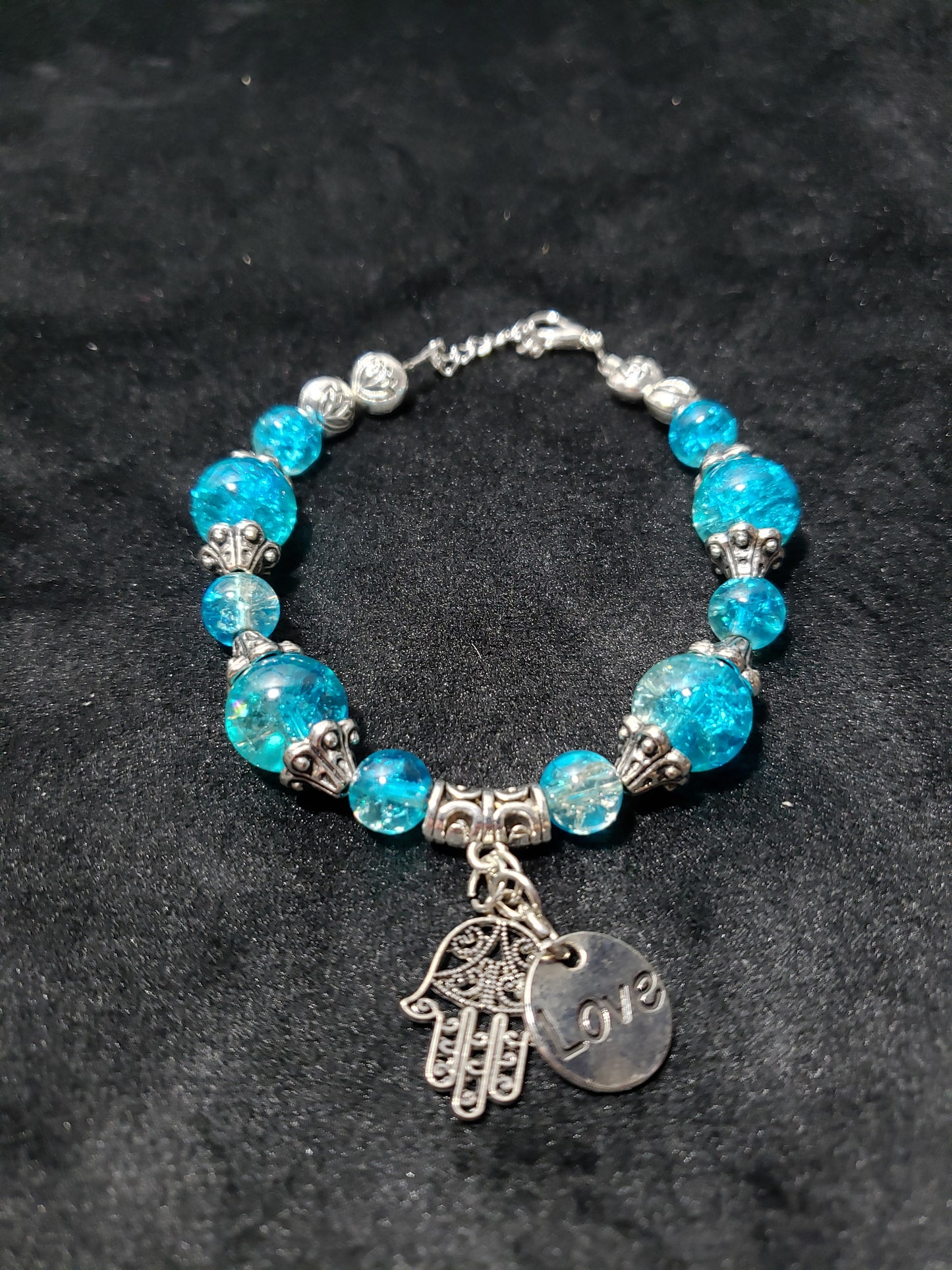 Blue crackle beaded bracelet with a silver charm on a black background