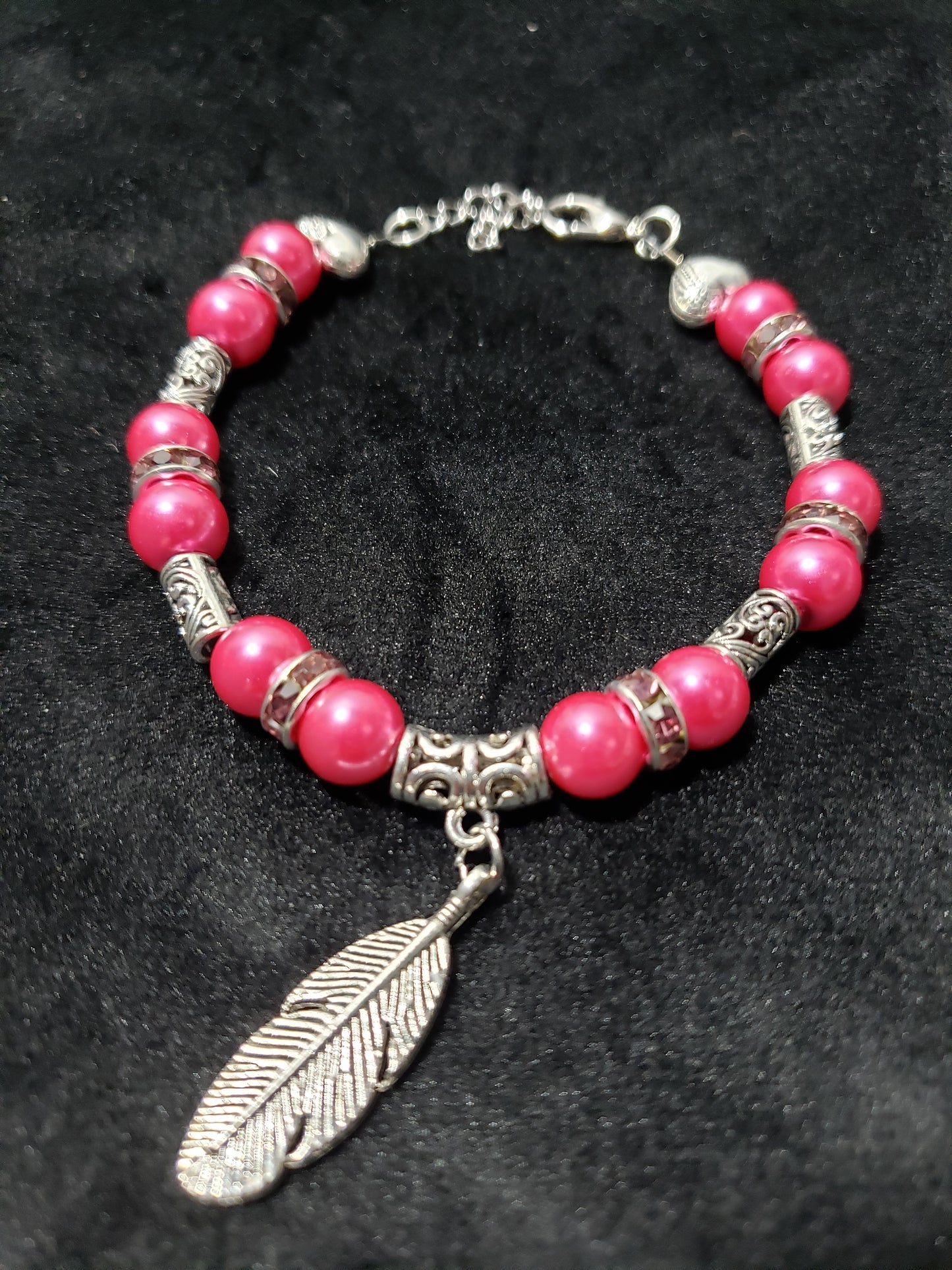 Bracelet with fuchsia beads and silver feather charm on a dark background