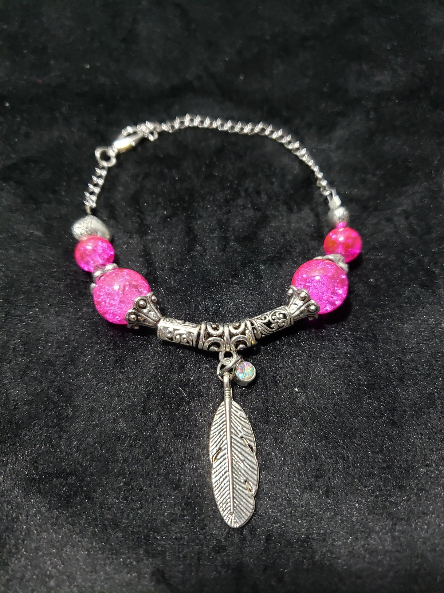 Bracelet with pink beads and a silver feather charm on a dark background