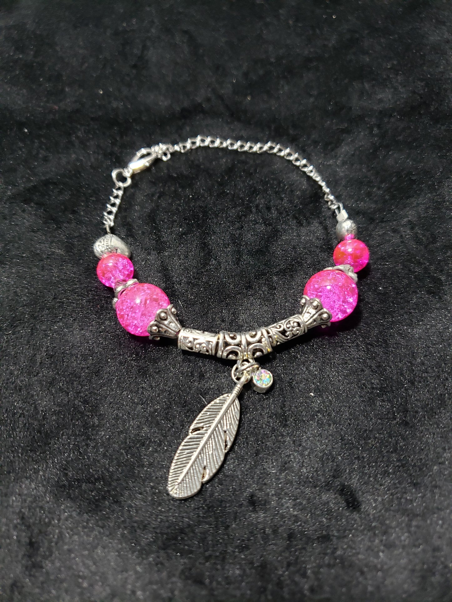 Bracelet with pink beads and silver feather charm on a dark background