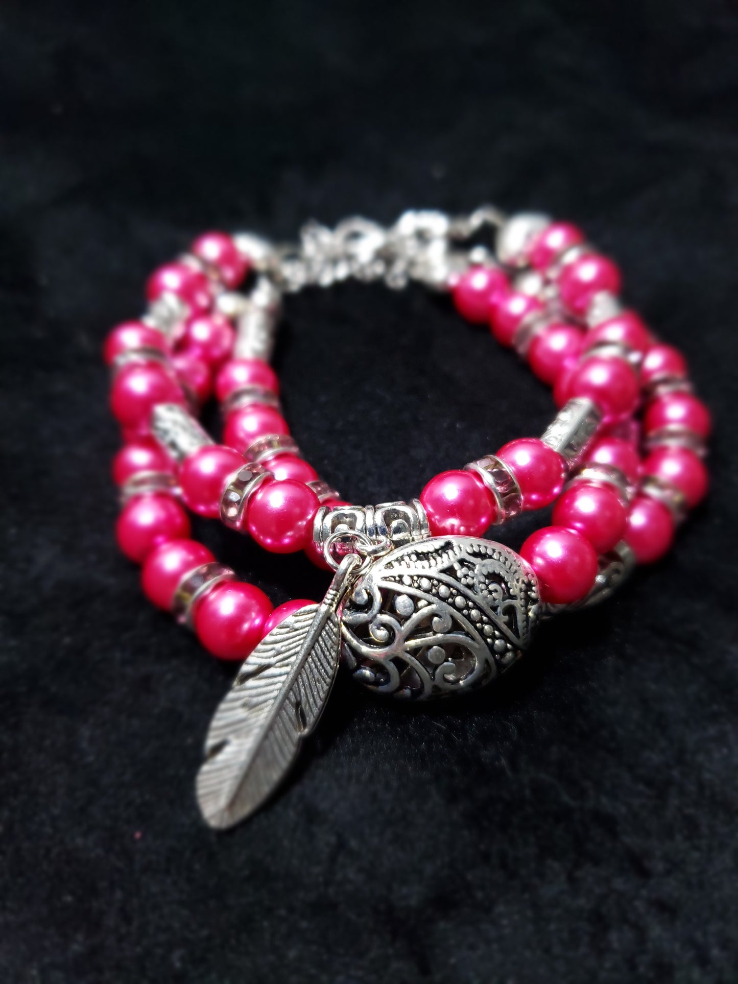 Fuchsia beaded bracelet with a silver feather charm on a black background