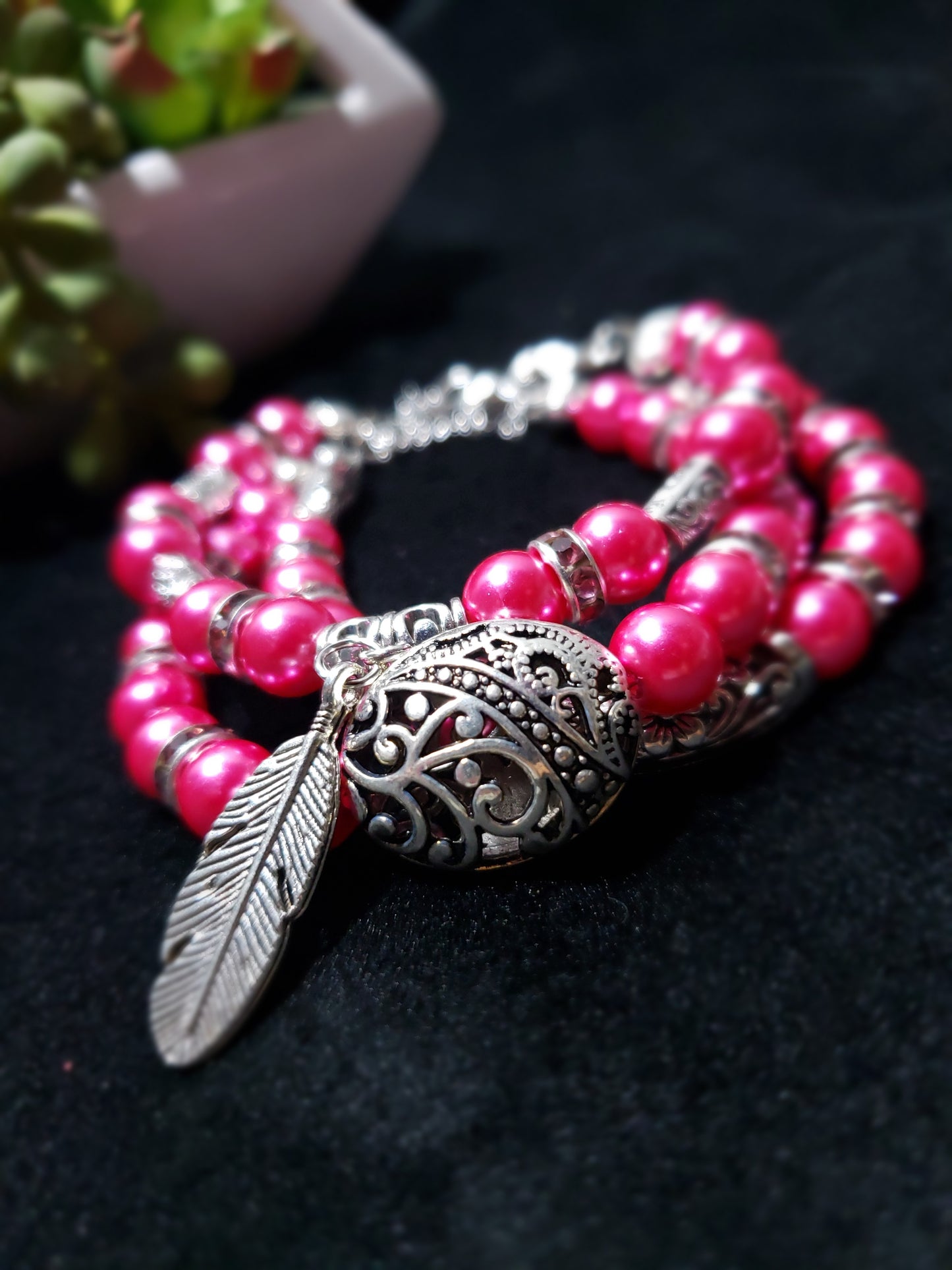 Fuchsia beaded bracelet with silver feather and decorative clasp on a dark background