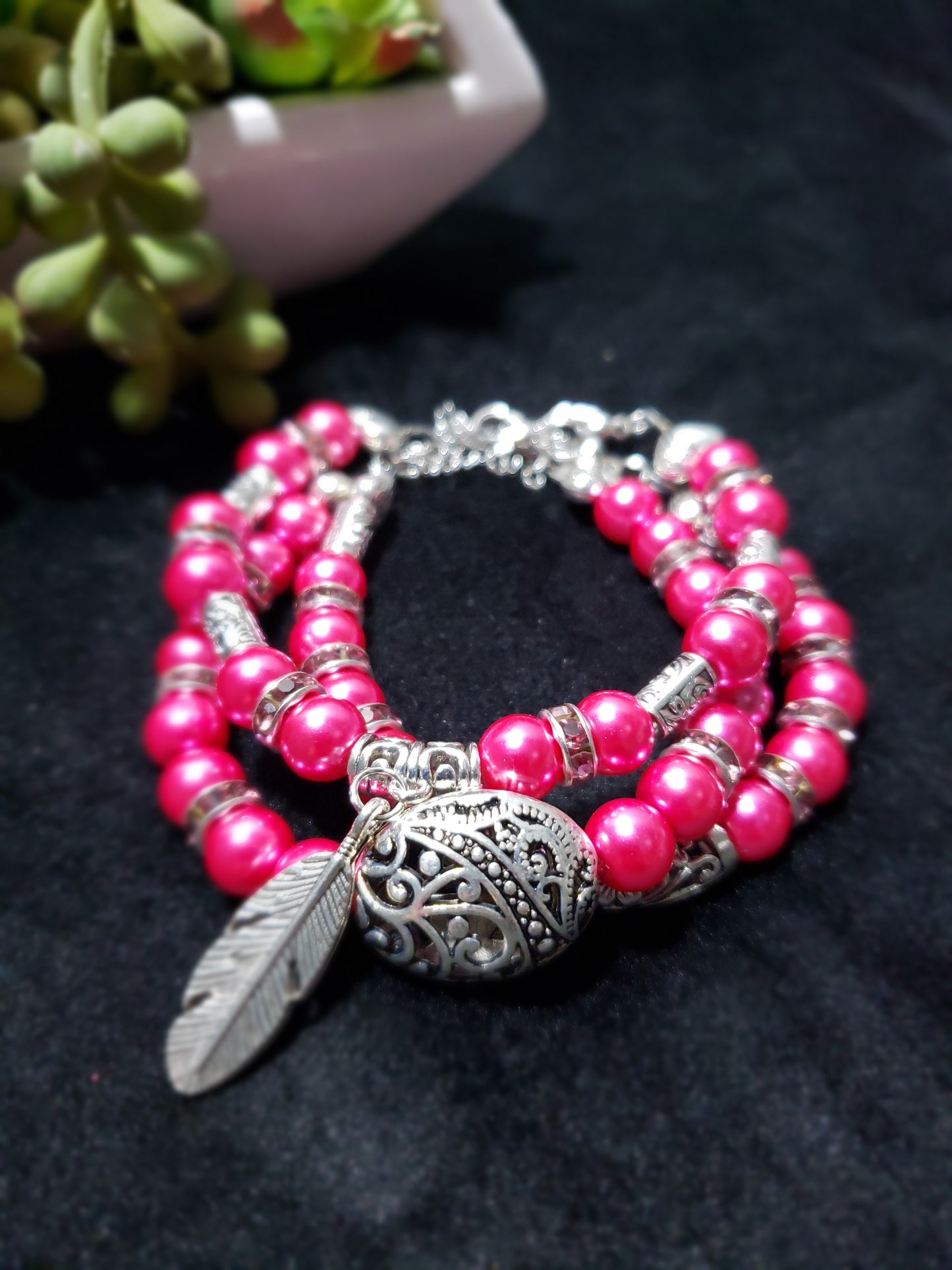 Fuchsia beaded bracelets with silver feather charm on a dark background