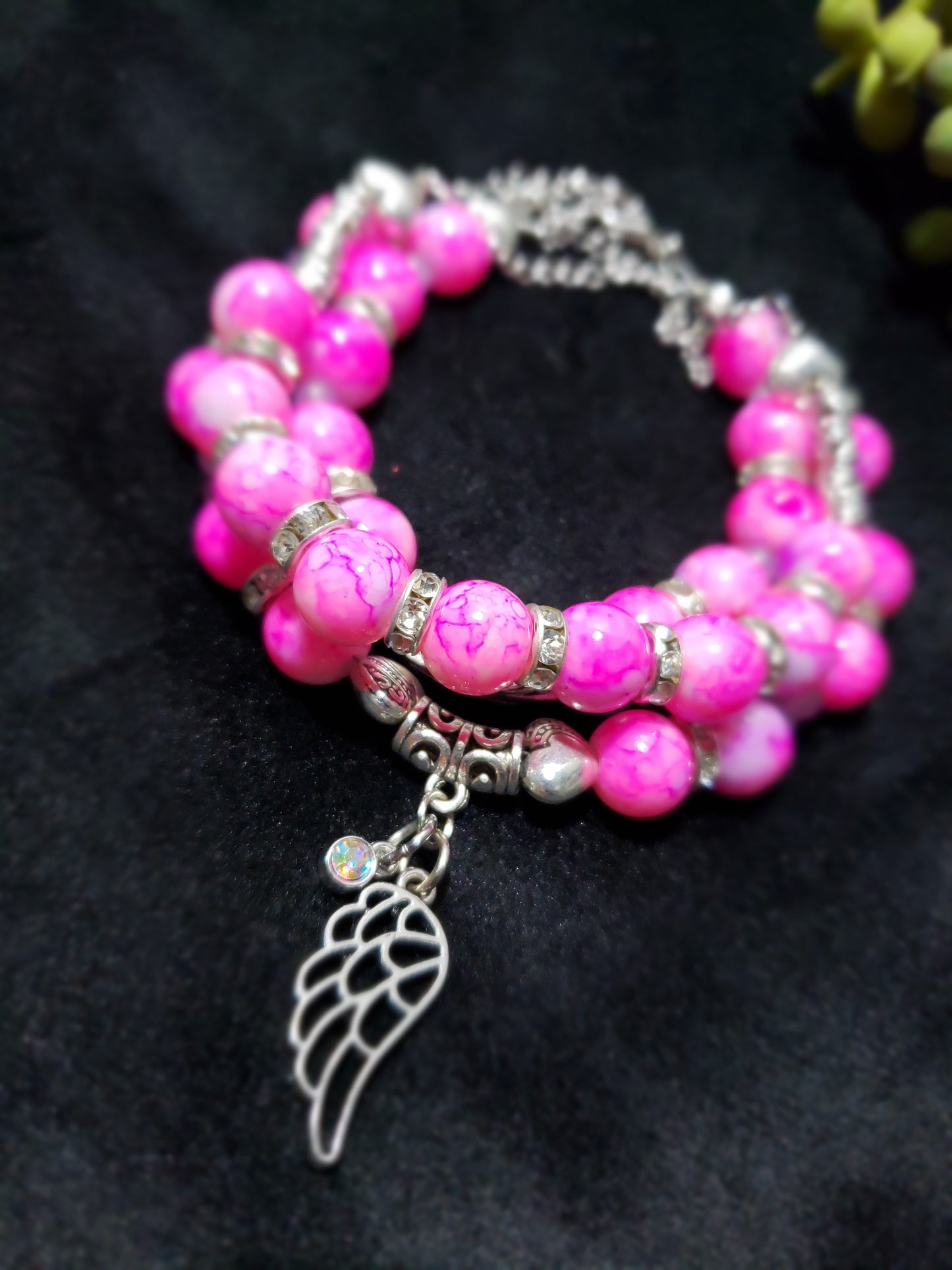 Pink beaded bracelet with a silver wing charm on a dark background
