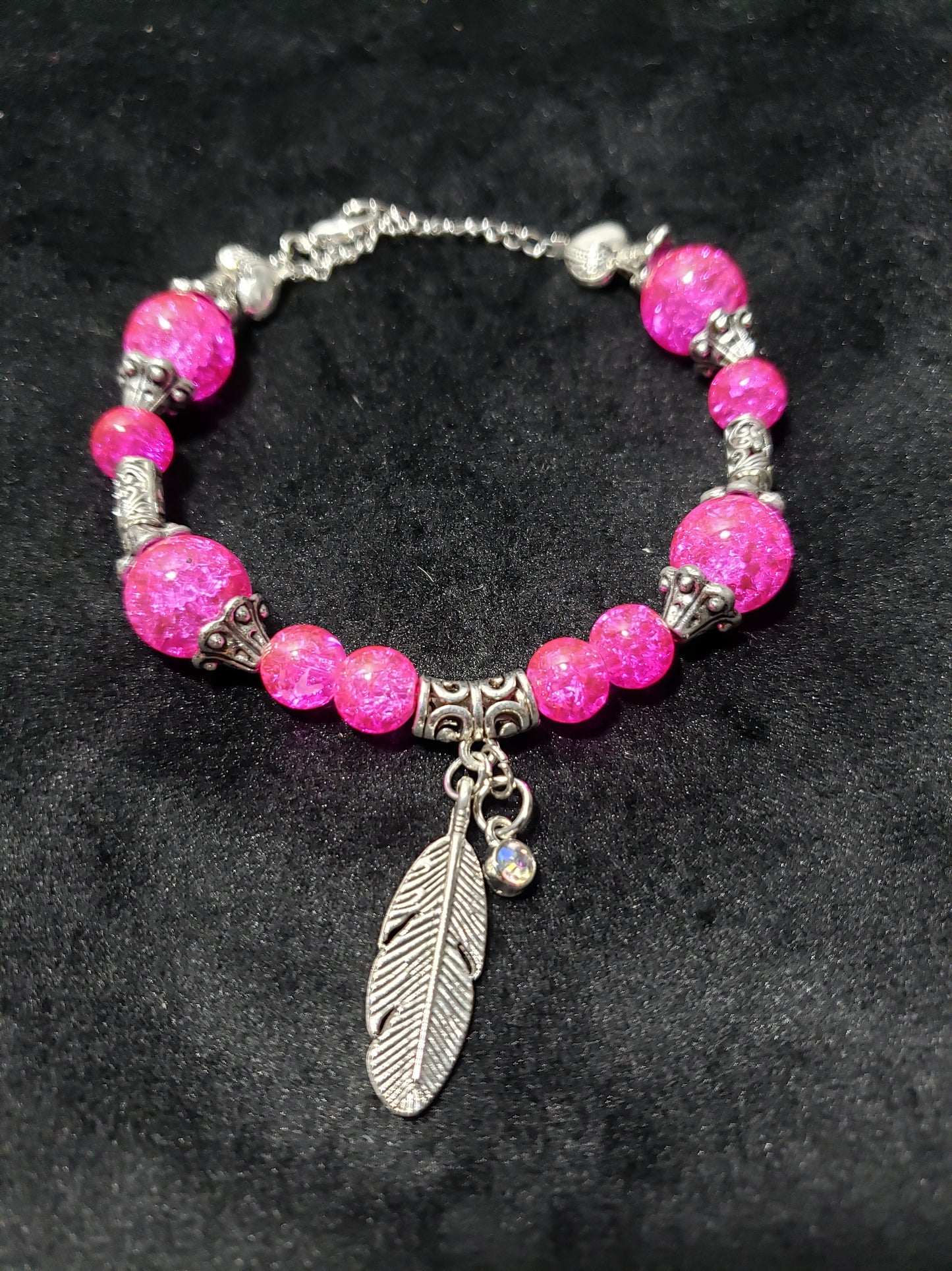 Pink beaded bracelet with silver accents and a feather charm on a dark background