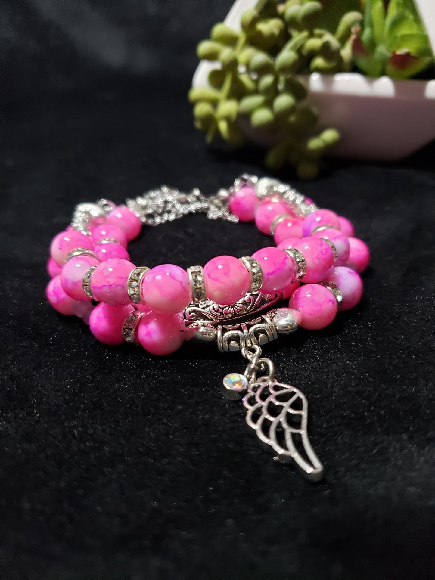 Pink beaded bracelet with a silver charm on a dark background