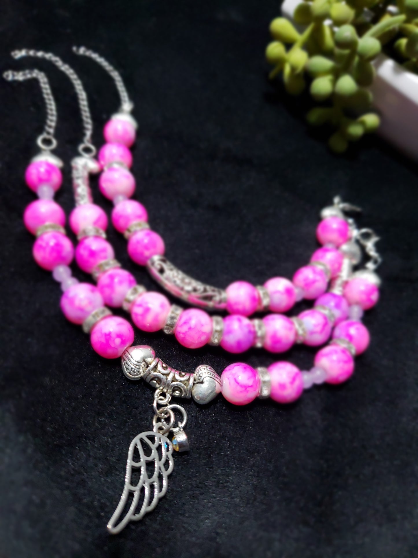 Pink marble beaded bracelet with silver angel wing charm on a black background