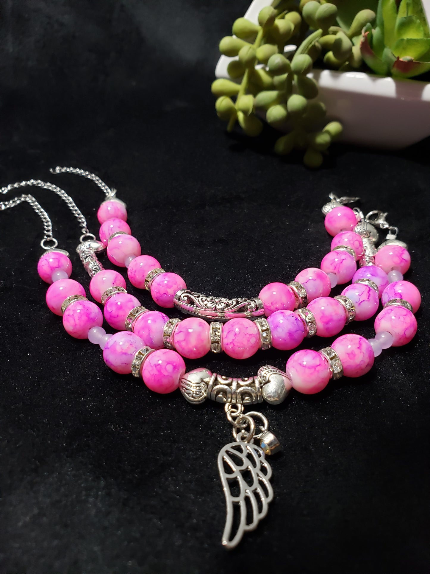 Pink marble beaded bracelet with silver angel wing charm on a black background