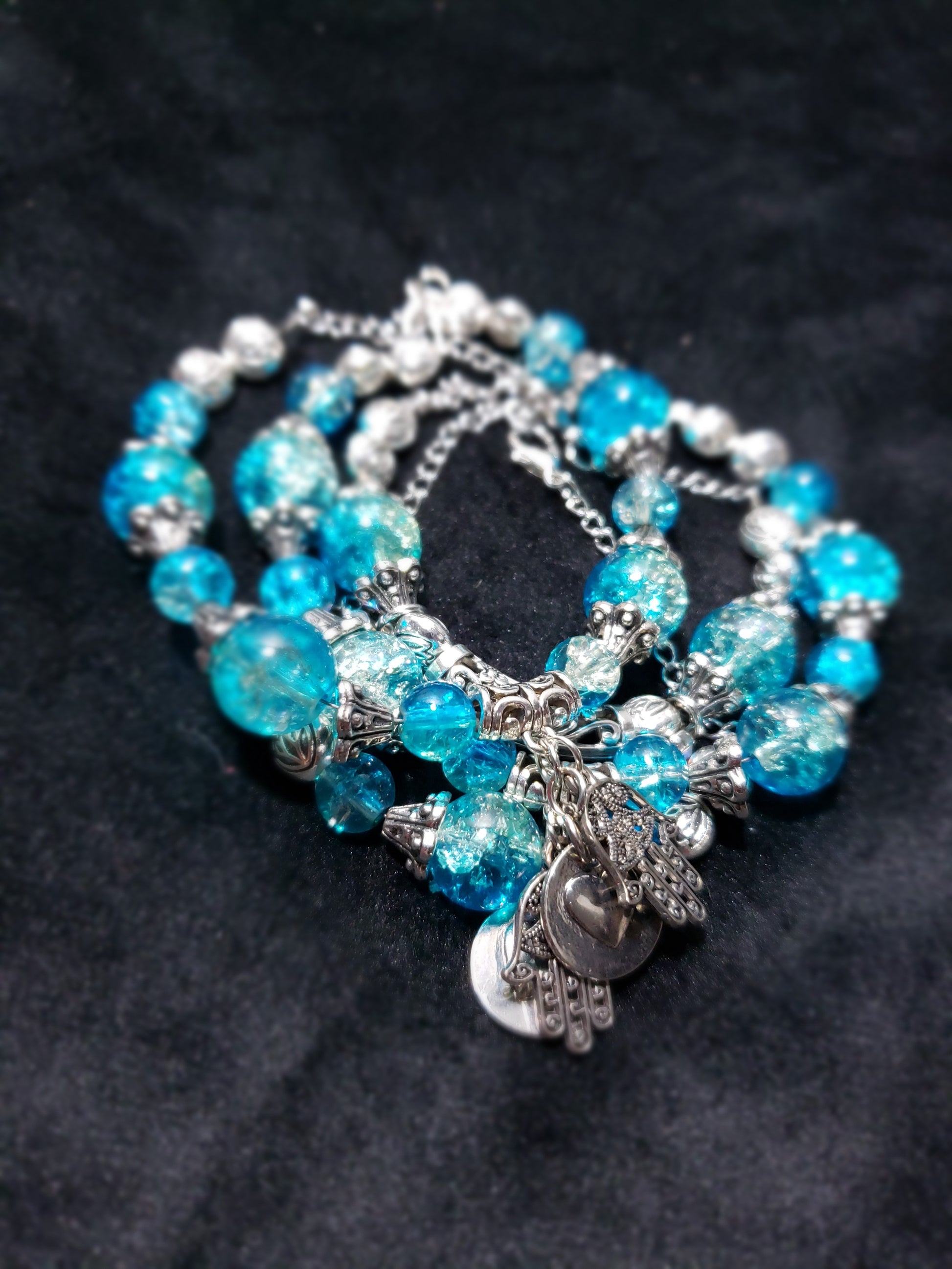 Blue Crackle beaded bracelet with silver charms on a dark background
