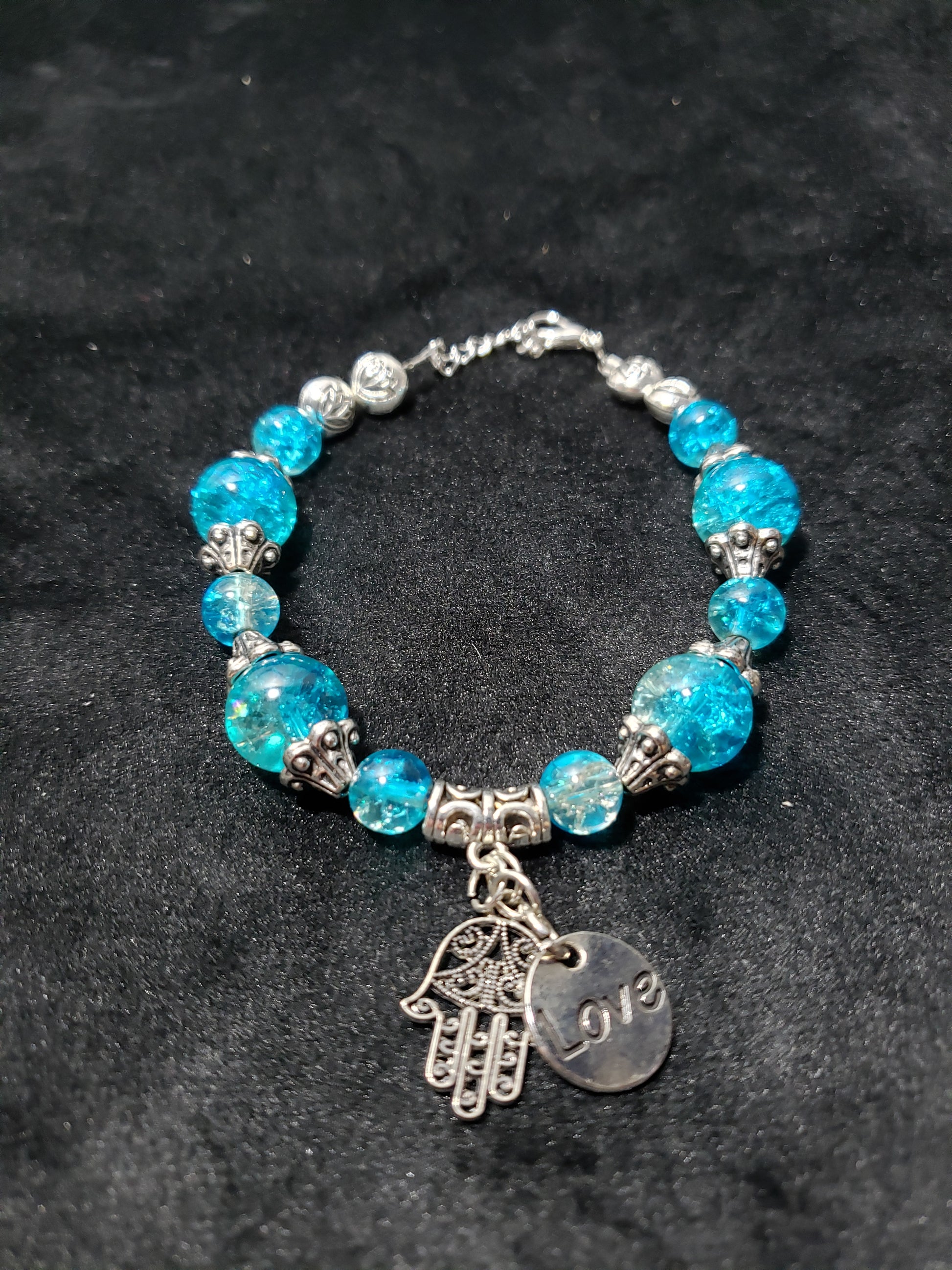 Blue crackle beaded bracelet with a silver charm on a black background
