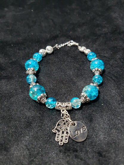 Blue crackle beaded bracelet with a silver charm on a black background