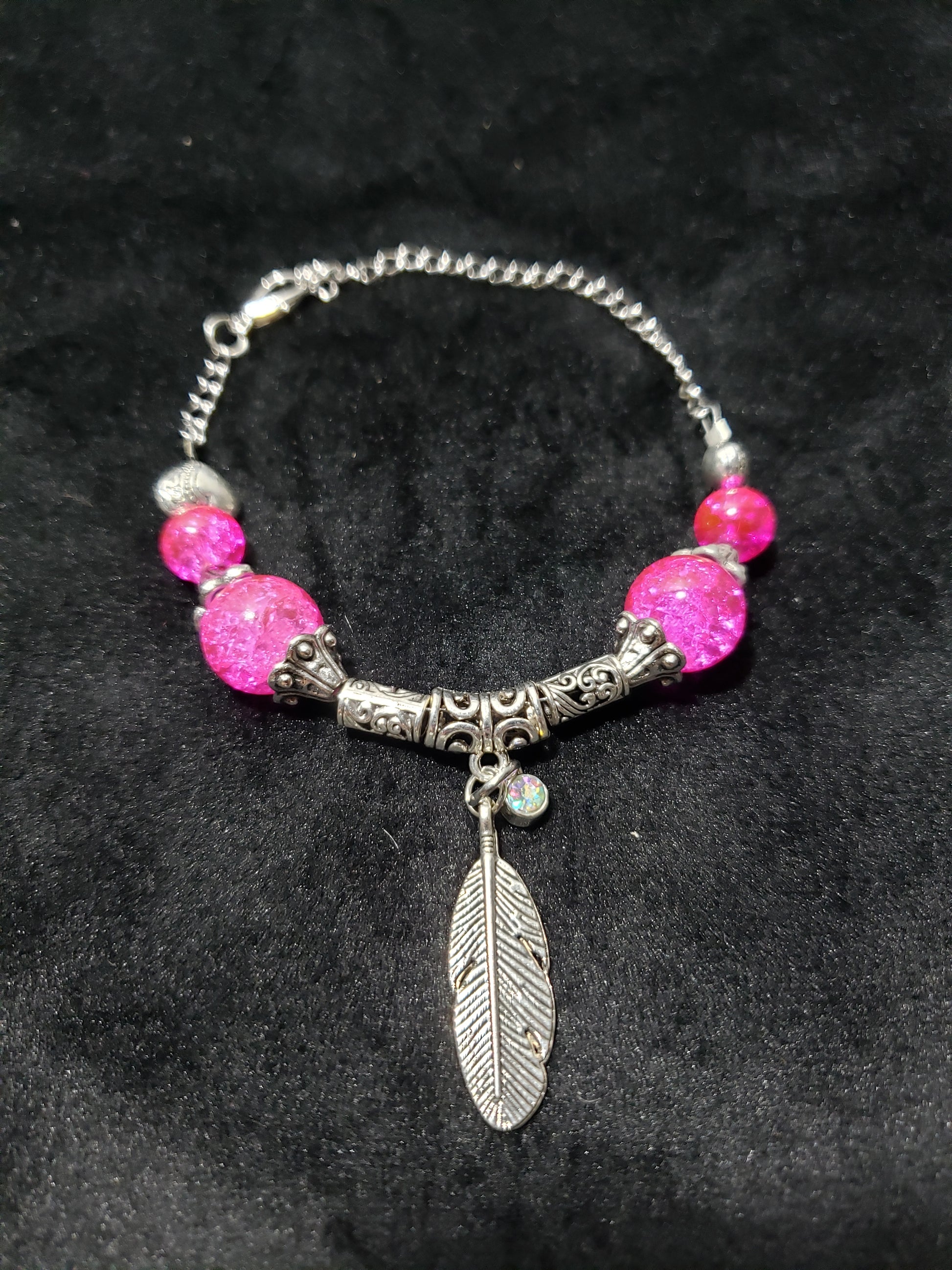 Bracelet with pink beads and a silver feather charm on a dark background