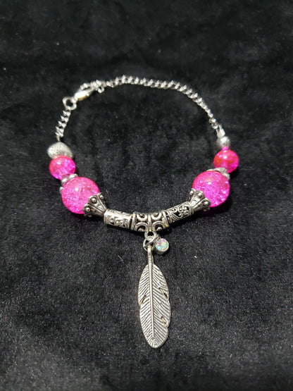 Bracelet with pink beads and a silver feather charm on a dark background