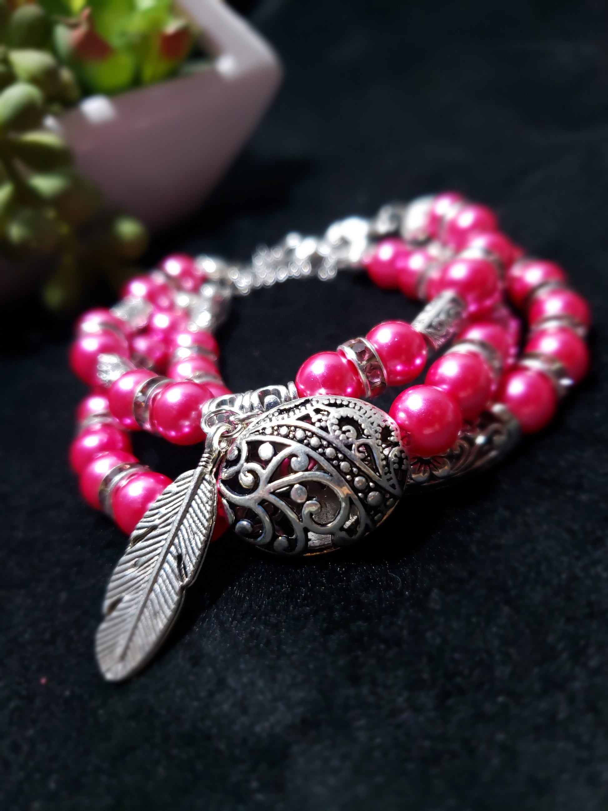 Fuchsia beaded bracelet with silver feather and decorative clasp on a dark background
