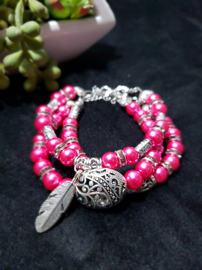 Fuchsia beaded bracelets with silver feather charm on a dark background