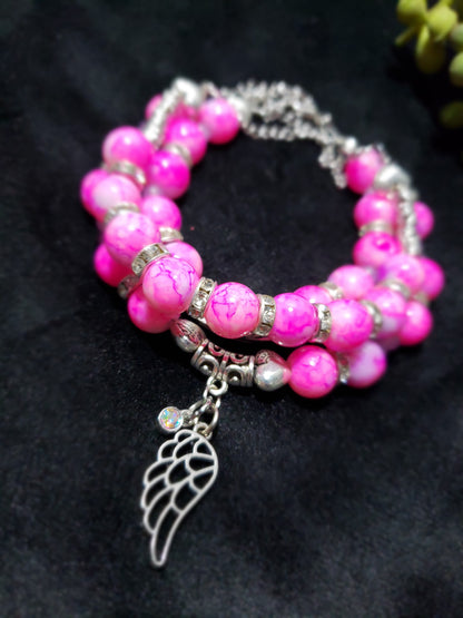 Pink beaded bracelet with a silver wing charm on a dark background