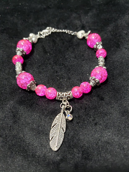Pink beaded bracelet with silver accents and a feather charm on a dark background