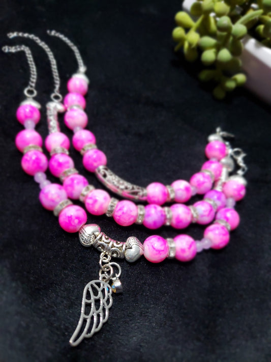 Pink marble beaded bracelet with silver angel wing charm on a black background
