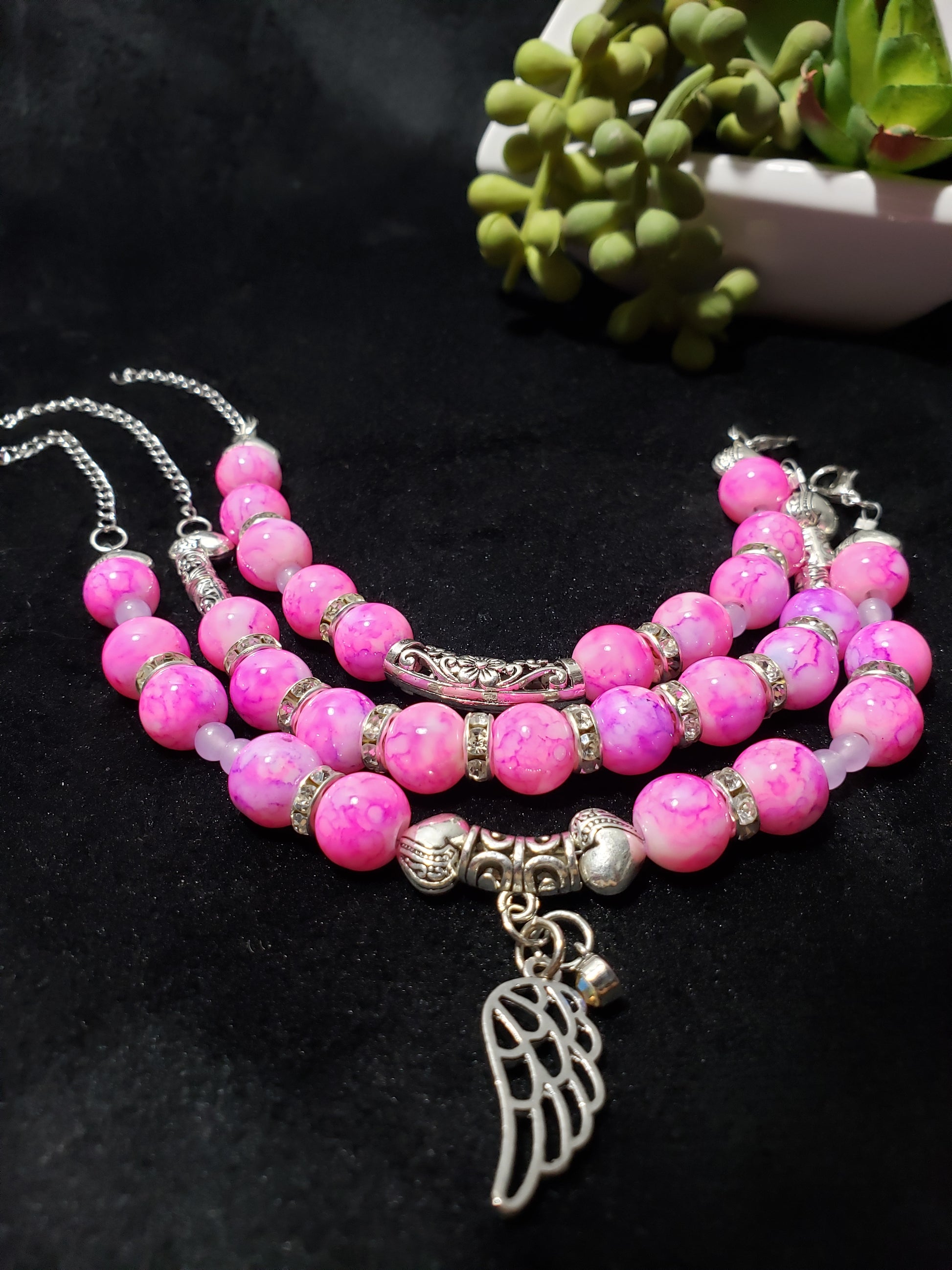 Pink marble beaded bracelet with silver angel wing charm on a black background