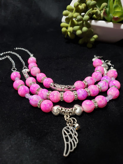 Pink marble beaded bracelet with silver angel wing charm on a black background