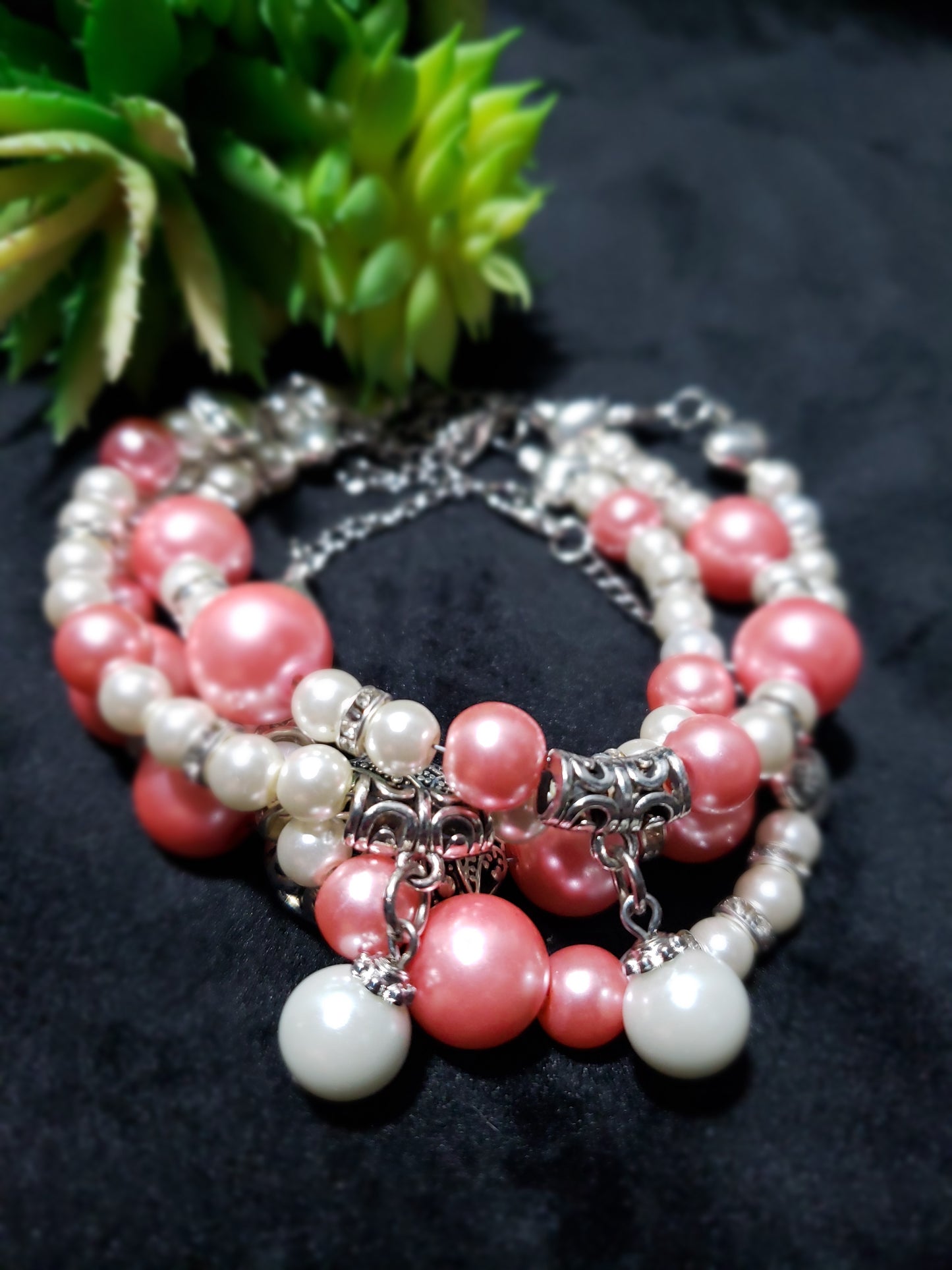 Stack of pink and white beaded bracelets with silver charms on a dark background